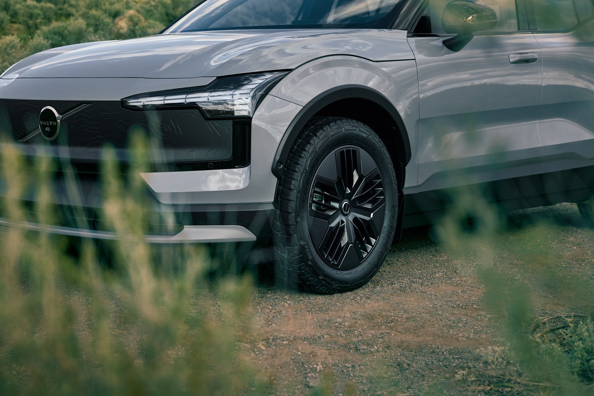 Nærbilde av Volvo EX30 Cross Country skrått forfra med gress i forgrunnen med fokus på felger og detaljer i fronten på bilen