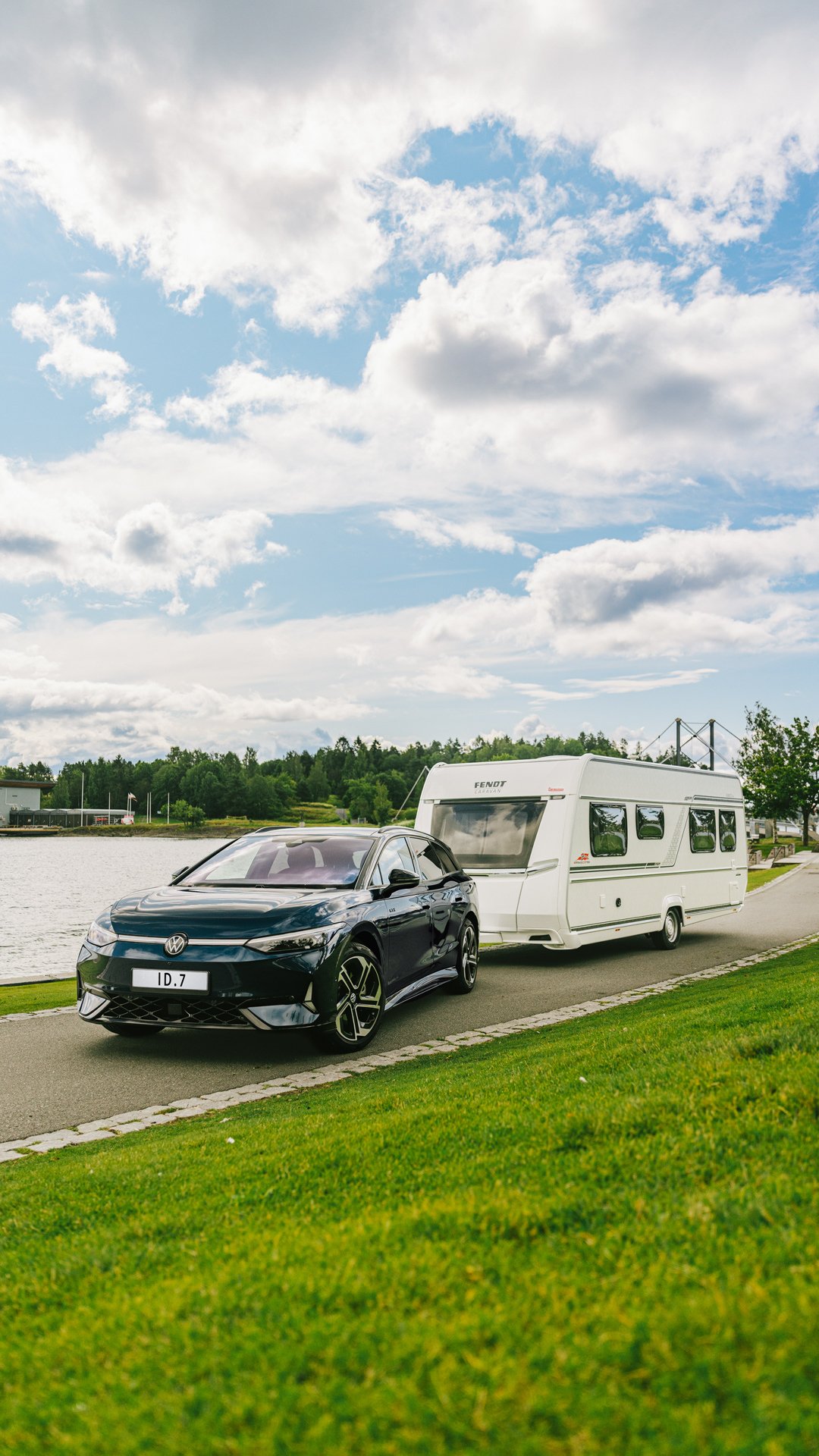 En blå Volkswagen ID.7 med campingvogn parkert foran et vann