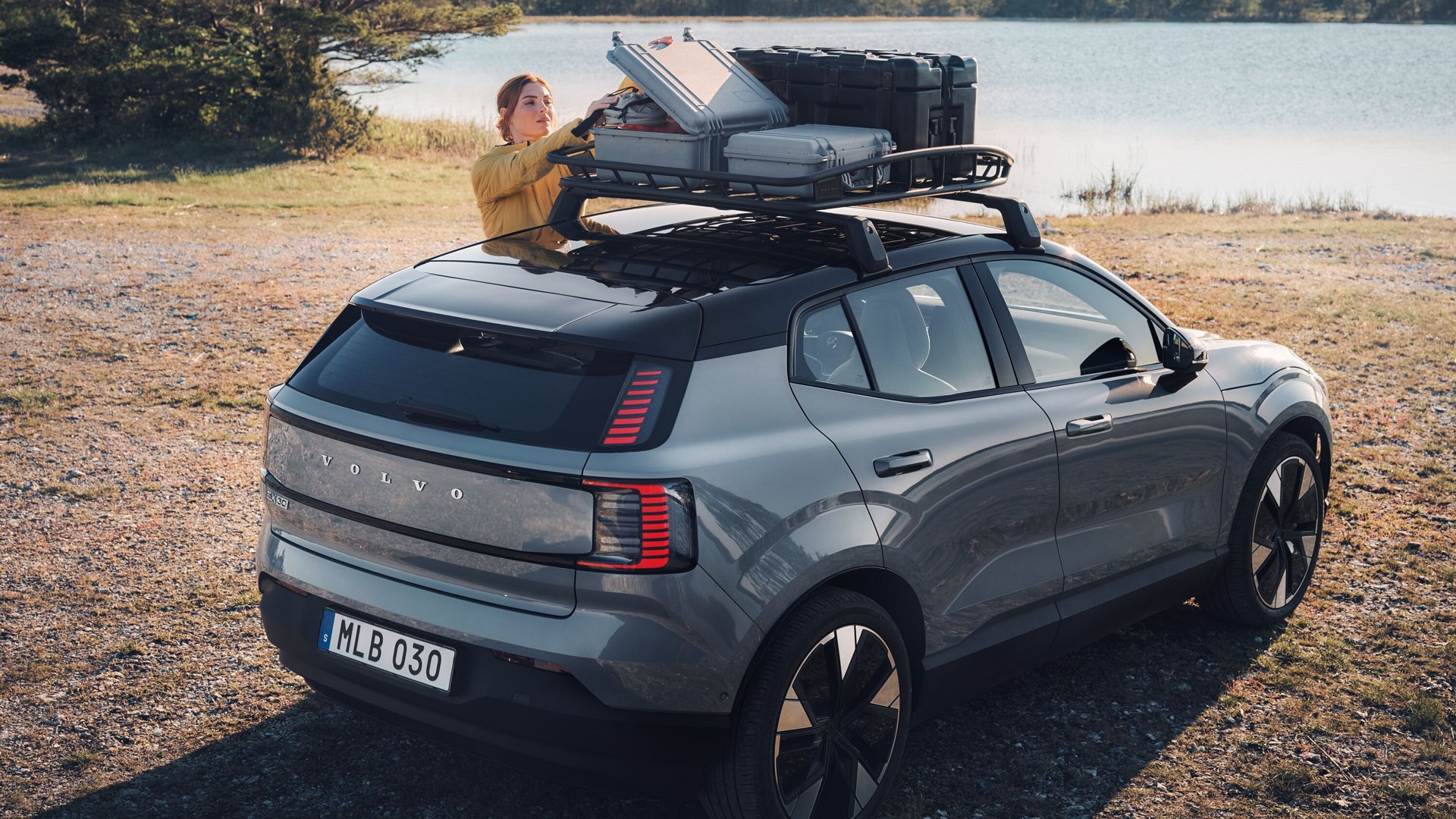 Volvo EX30 parkert foran et vann mens en dame henter noe fra en koffert på takgrinden,