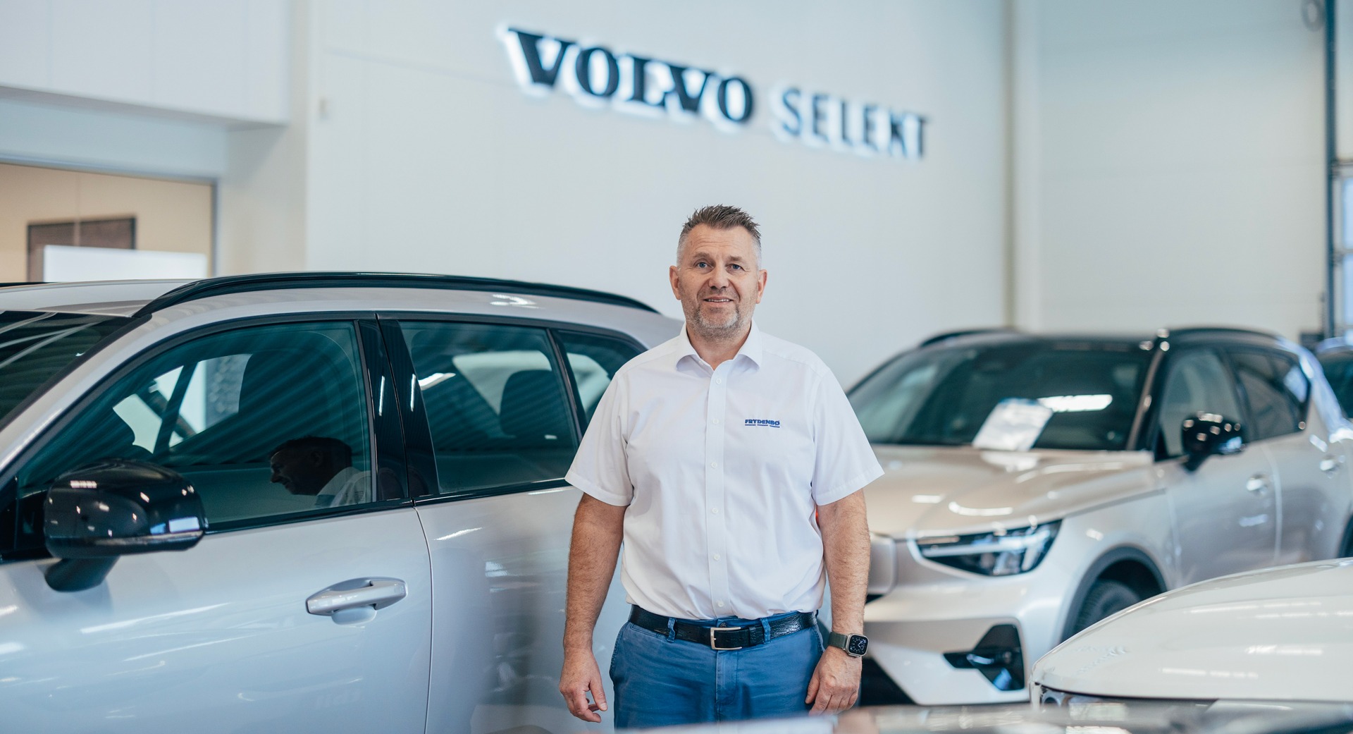 En smilende bruktbilselger foran flere Volvo modeller hos FRydenbø Bil Mandal