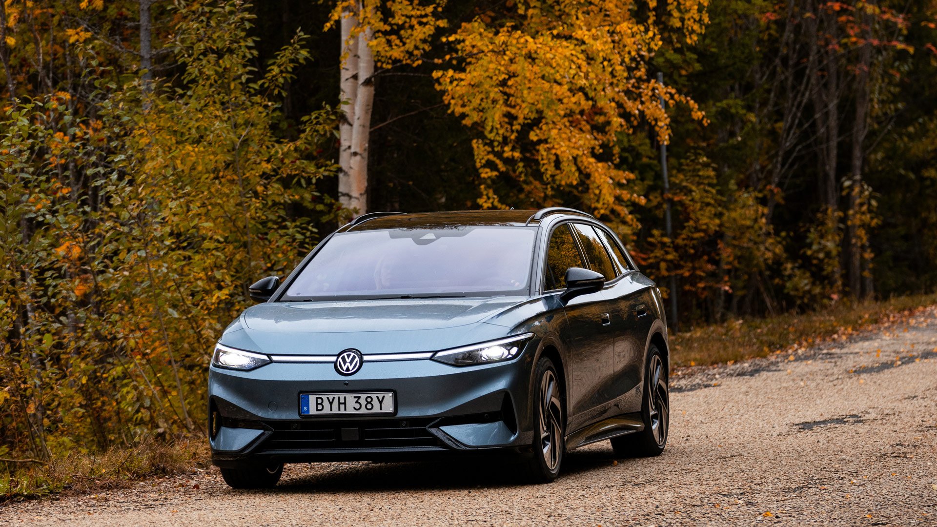 En blå VW ID.7 langs en grusvei med høstfargede trær i bakgrunnen