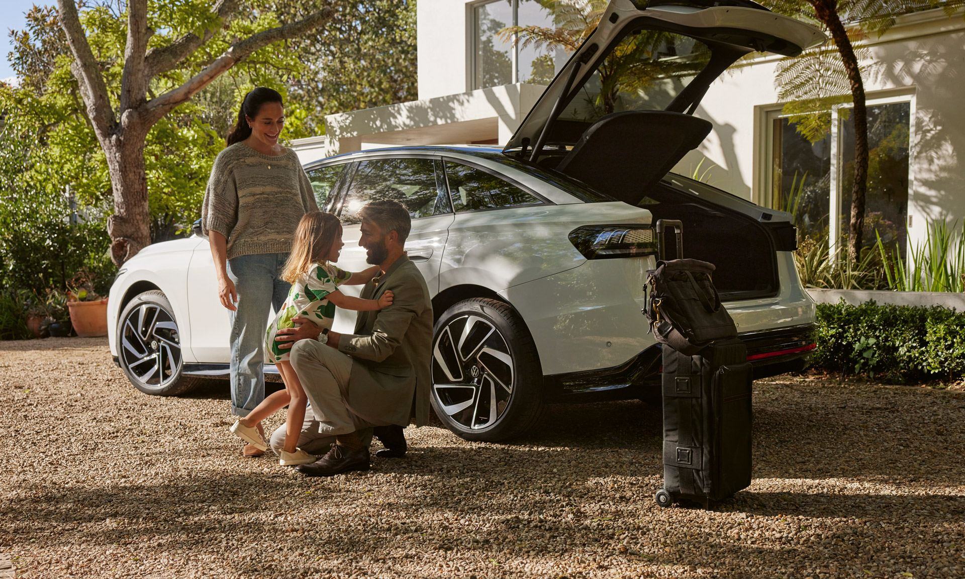 En far tar i mot et barn utenfor bilen mens en dame ser på.