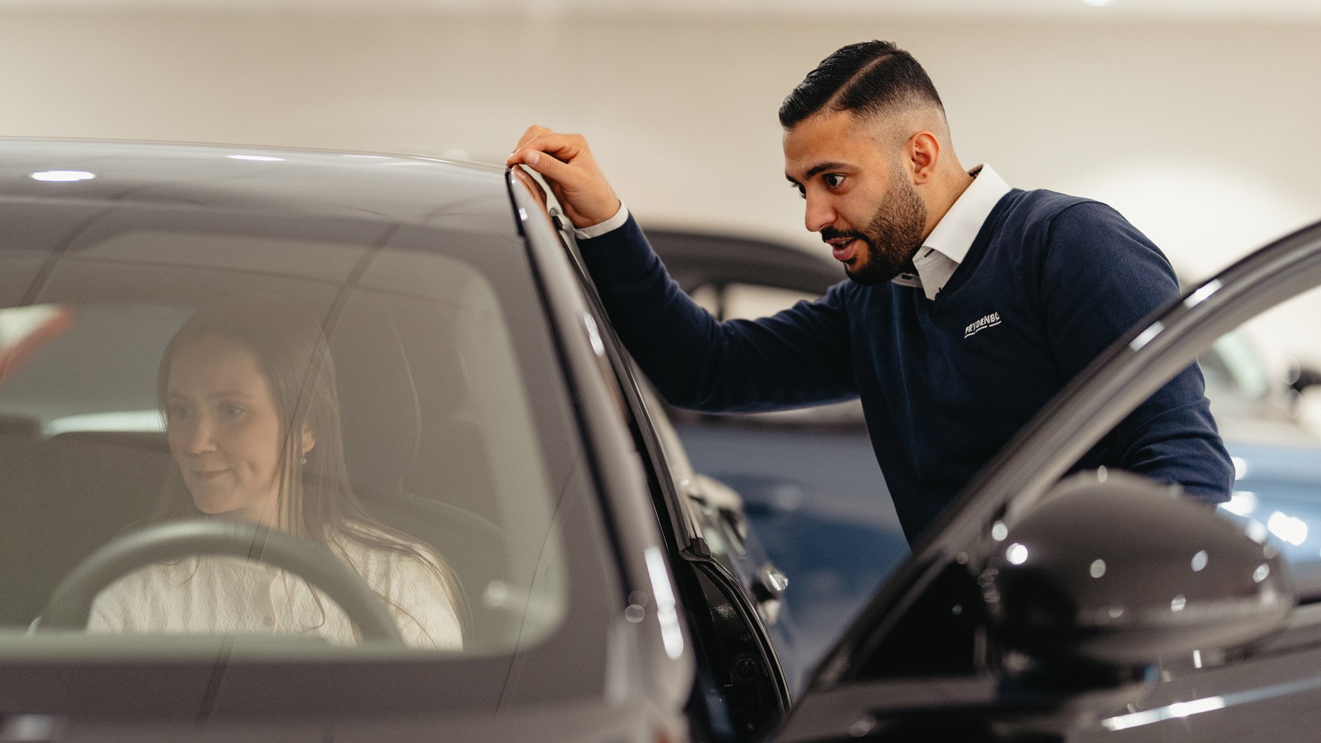 En bruktbilselger hjelper en kunde som sitter i bilen mens han står utenfor døren
