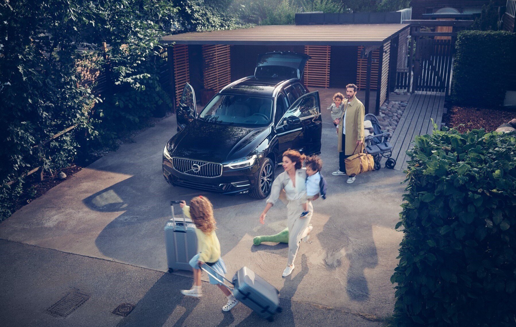 En familie pakker bilen for sommerferien. Det er kros på parkeringsplassen med løpende unger og bagasje. 