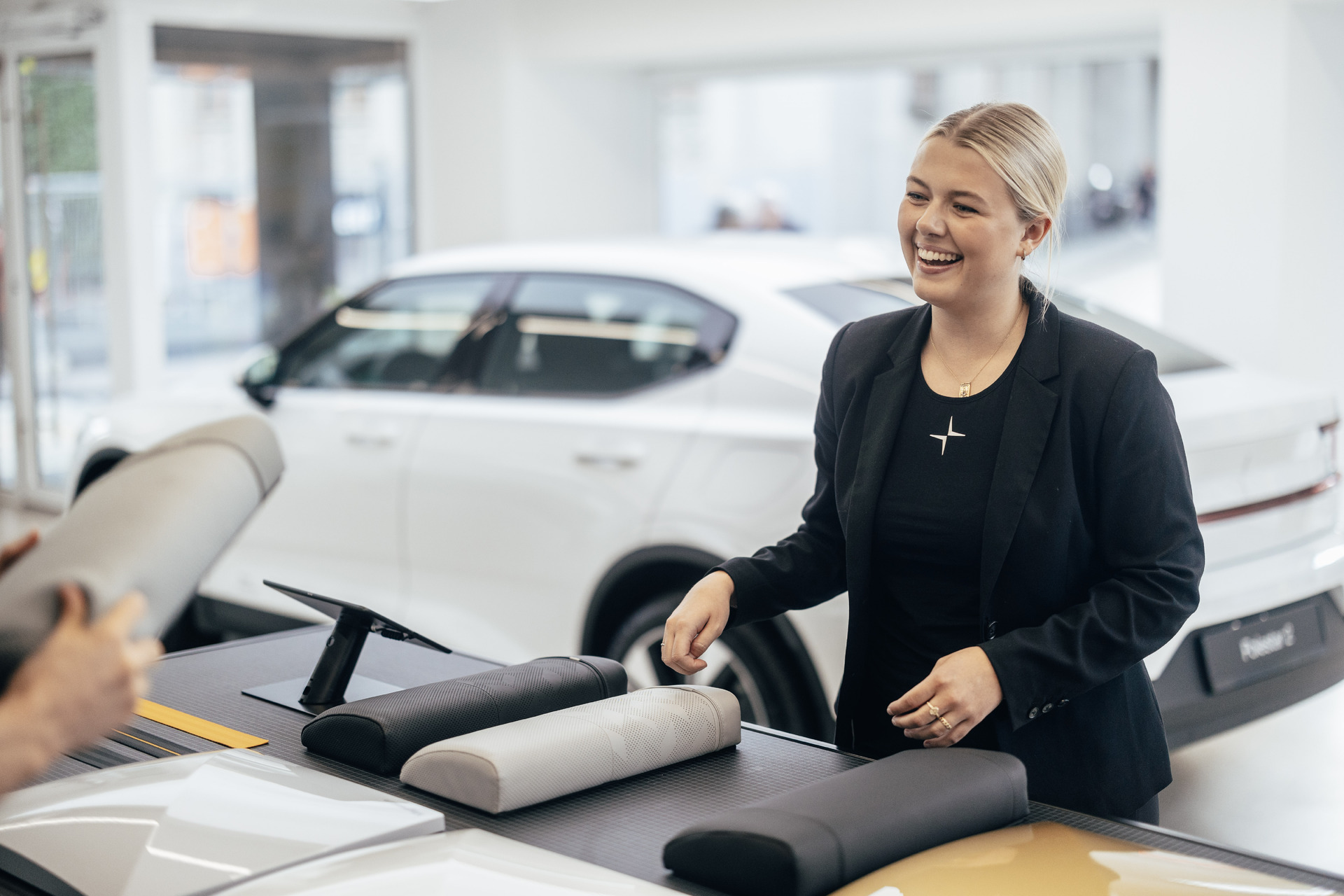 En Polestar selger smiler i Frydenbø Bils Polstar Space med en hvit Polestar 2 i bakgrunnen