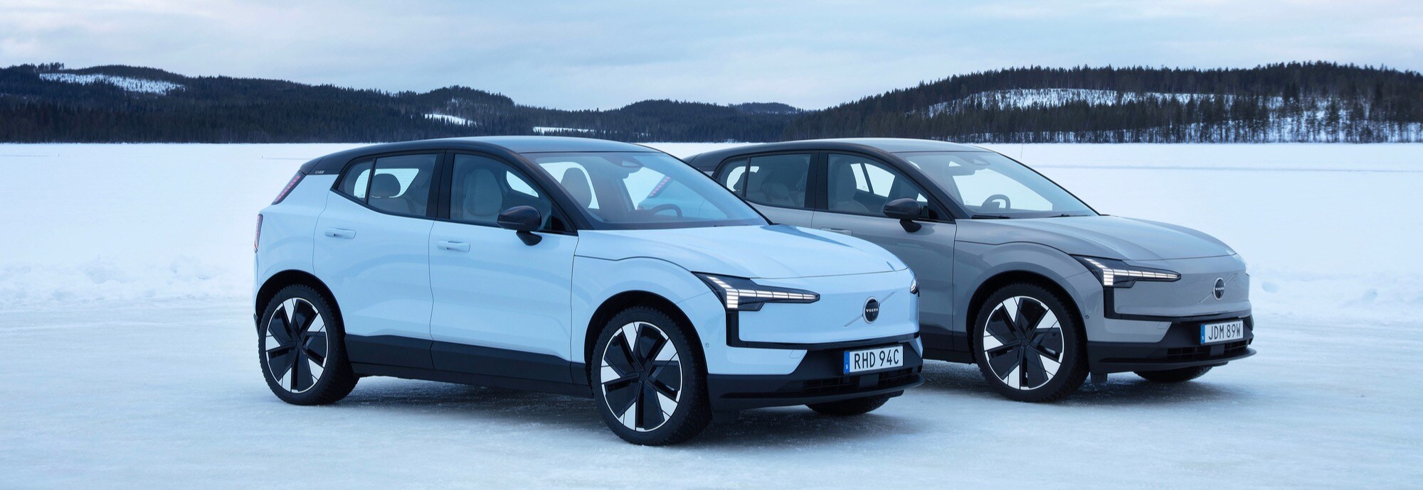 To, fine Volvo EX30-modeller parkert ved siden av hverandre i et vakkert snølandskap. 