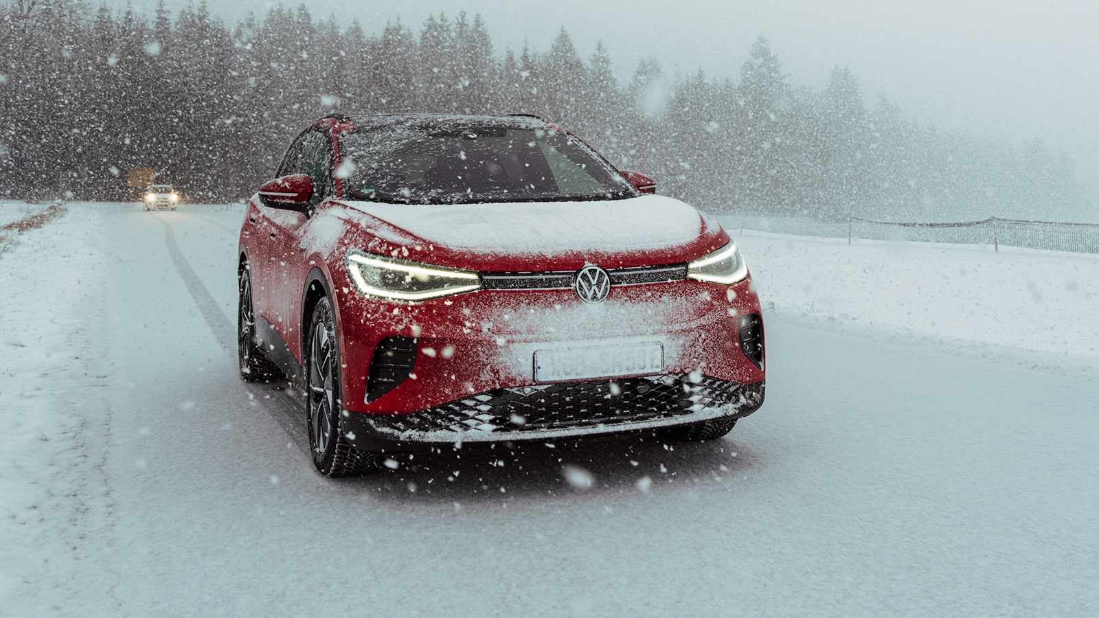En rød volkswagen kjører mot kamera i tett, hvit snø. 