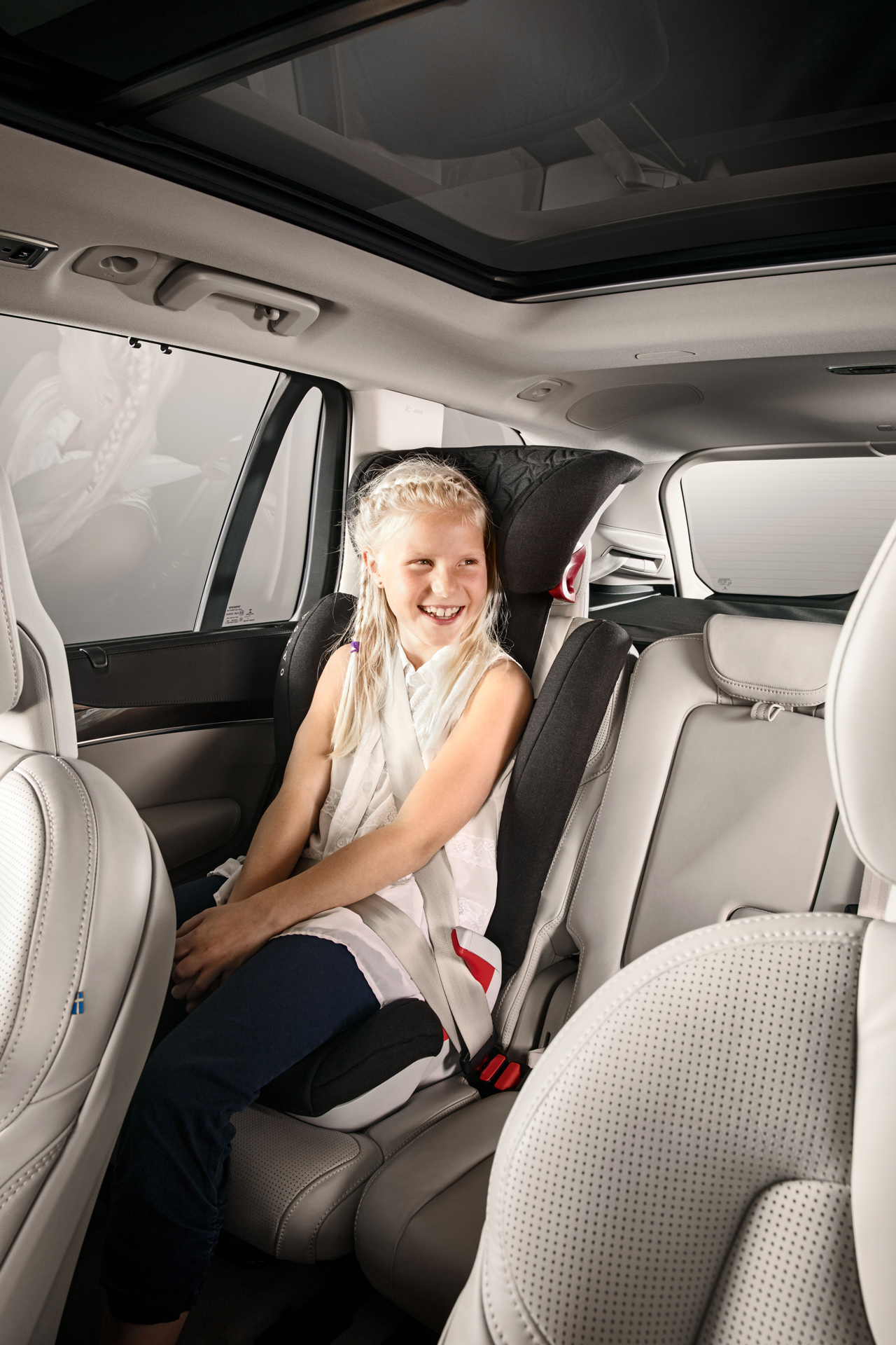 En jente sitter i et barnesete i baksetet på en bil og smiler