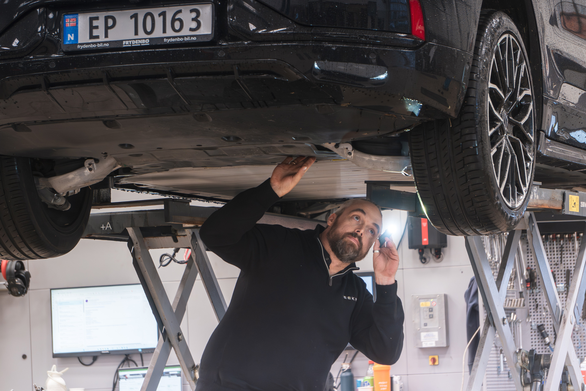 En zeekr mekaniker jobber under en Zeekr 001 som står på løftebukk og sjekker hjuloppheng
