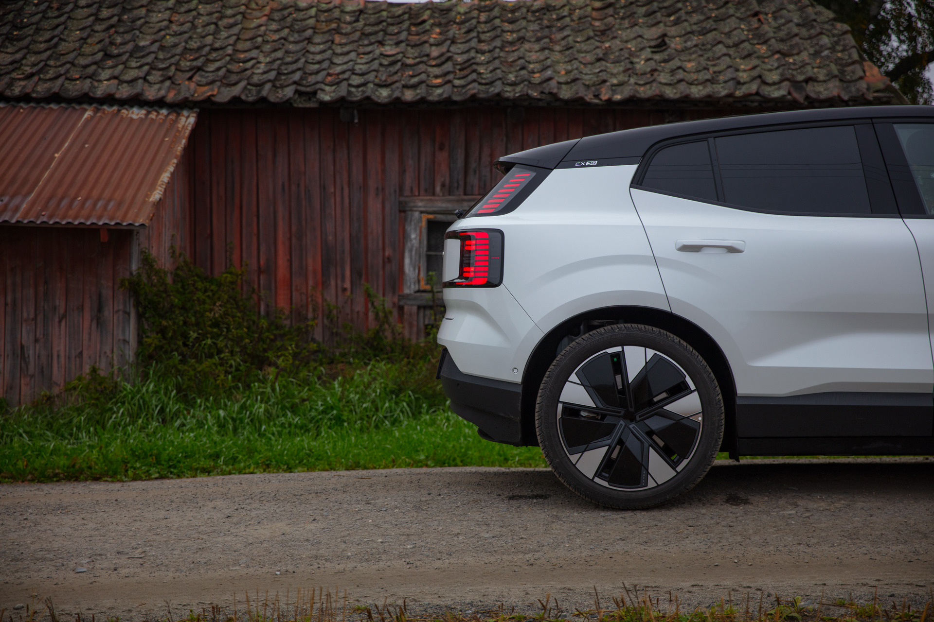 Bakenden på en Volvo EX30 sett fra siden med et gammelt hus i bakgrunnen