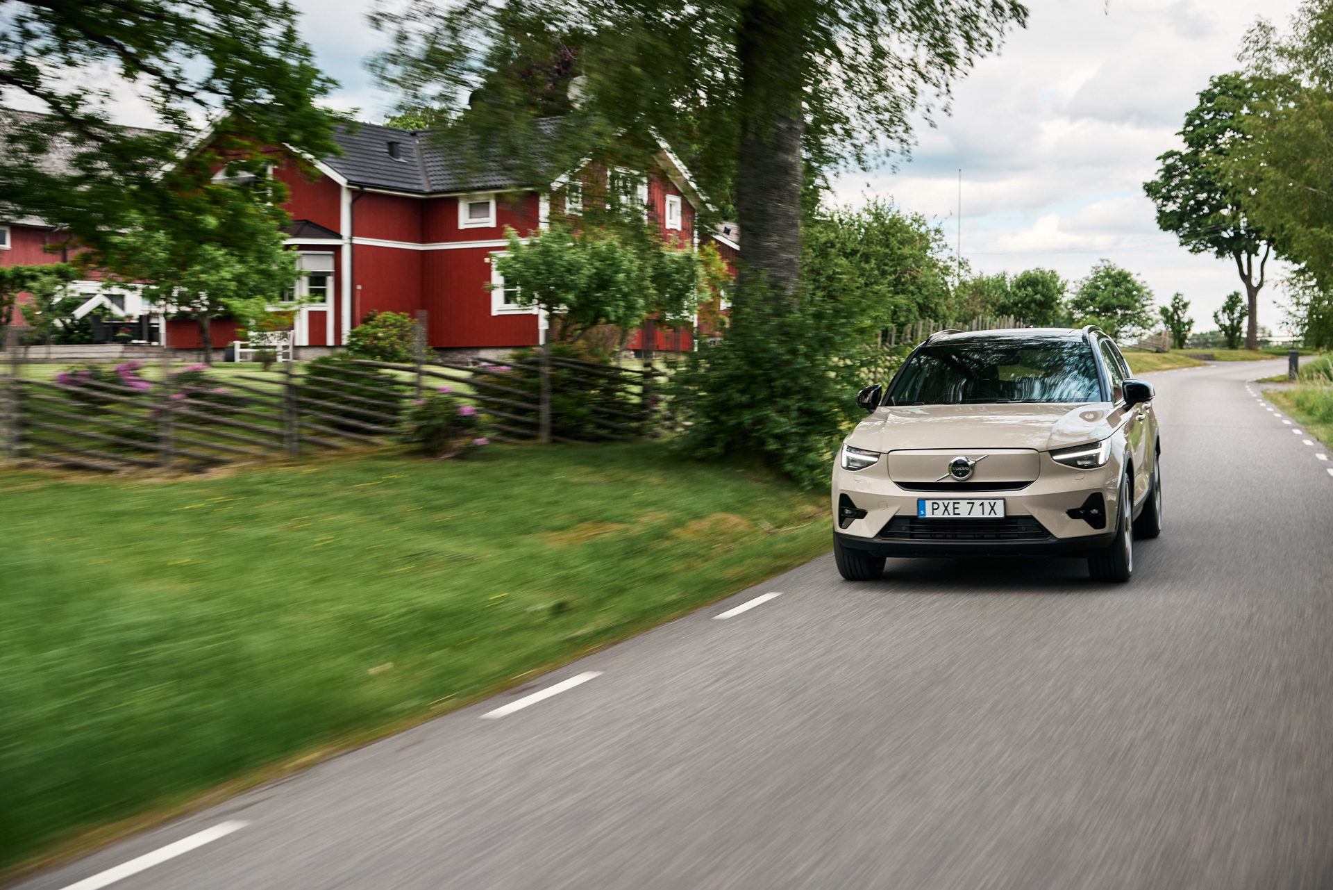 En Volvo EX40 kjører langs en svensk landevei med et rødt hus i bakgrunnen
