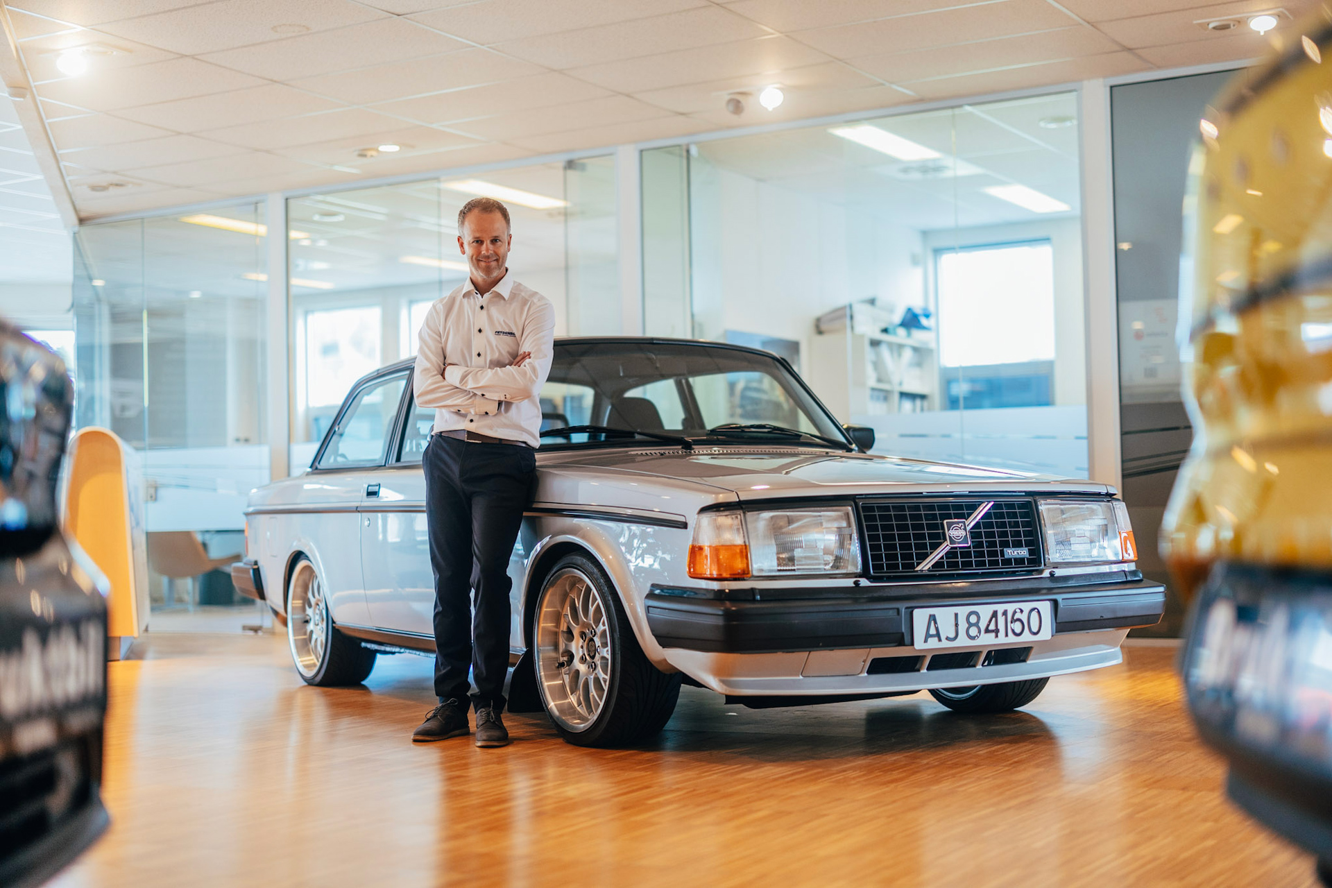 En bilselger smiler lent inntil en eldre Volvo i Frydenbø Bil sine lokaler i Kristiansand